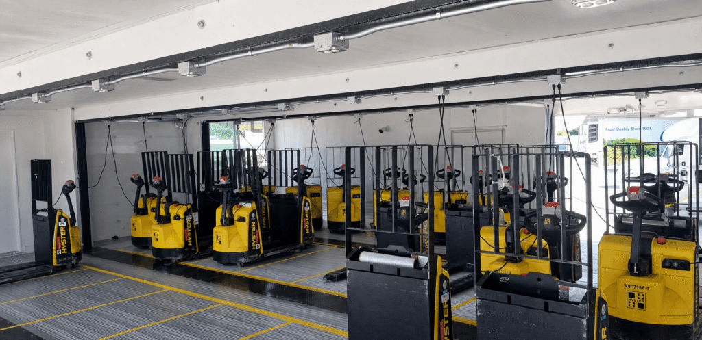 A row of yellow pallet jacks with black handles are neatly lined up in a well-lit, spacious indoor area. The scene appears organized and orderly.