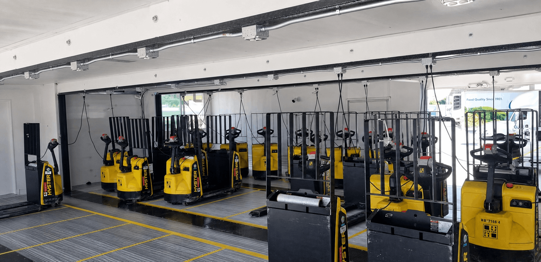 A row of yellow pallet jacks with black handles are neatly lined up in a well-lit, spacious indoor area. The scene appears organized and orderly.