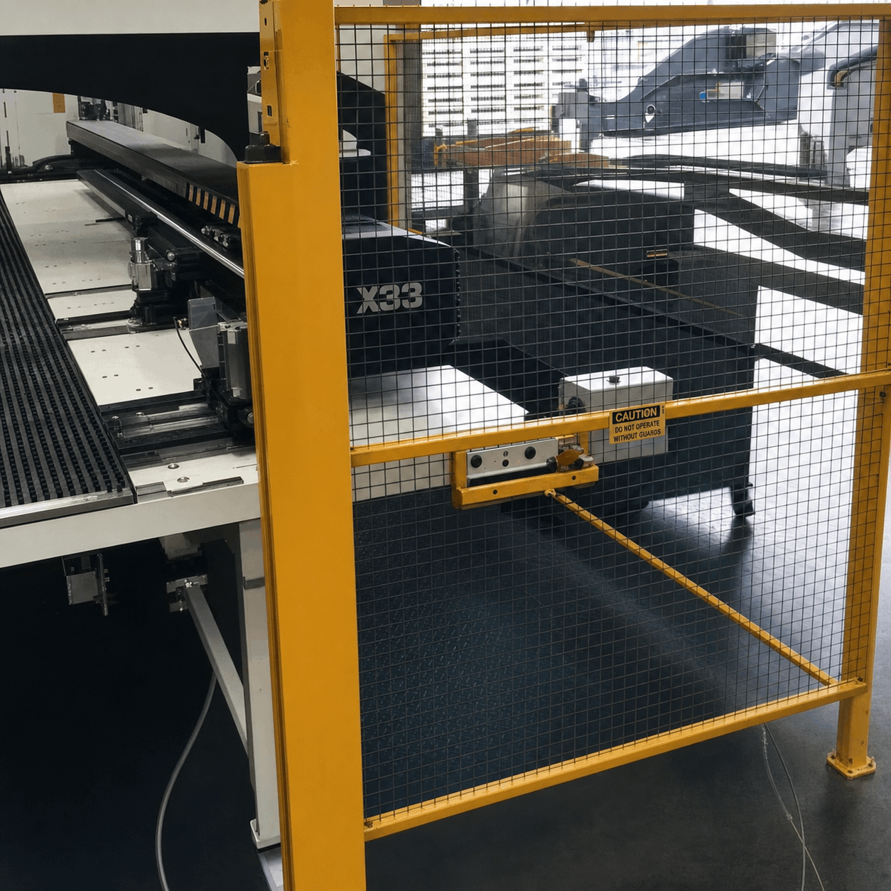 Large industrial machine behind yellow safety cage marked with "Caution" sign, suggesting restricted access. Steel components convey a mechanical, industrial vibe.
