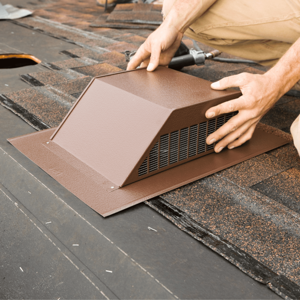 Hands installing a brown roof vent on shingles. The person is securing the vent, emphasizing home improvement and attention to detail in roofing work.
