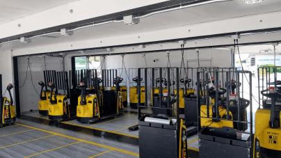 A row of yellow pallet jacks with black handles are neatly lined up in a well-lit, spacious indoor area. The scene appears organized and orderly.