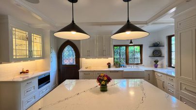 Bright kitchen with marble countertops, dark pendant lights, and a wooden arched door. A vase of flowers sits on the island, creating a cozy ambience.