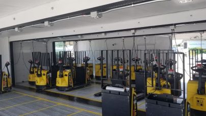 A row of yellow forklifts with protective cages are parked in a spacious, well-lit warehouse loading area. The scene conveys order and readiness.